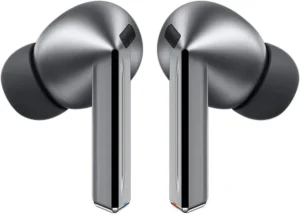 Renderização de estúdio de um par de Samsung Galaxy Buds 3 Pro, fones de ouvido sem fio premium na cor Titanium Gray, com design de haste elegante e acentos azuis e laranjas nas bases, exibidos lado a lado sobre um fundo branco.