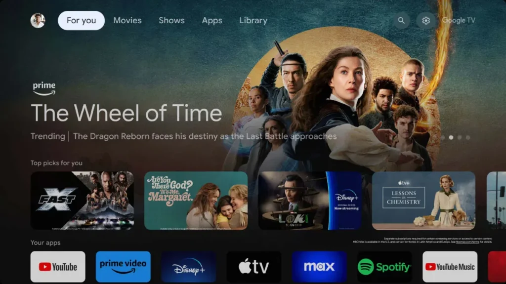 Interface da tela inicial do Google TV exibida na TV TCL C6K QD-Mini LED. A tela destaca recomendações de séries e filmes, além de atalhos para aplicativos populares de streaming como YouTube, Prime Video e Disney+, ilustrando a navegação e as funcionalidades extras do sistema inteligente.