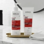 Frascos do Kit Vichy Dercos Antiqueda Energy+ com shampoo e condicionador apoiados sobre uma bancada de mármore claro em um banheiro elegante e minimalista.