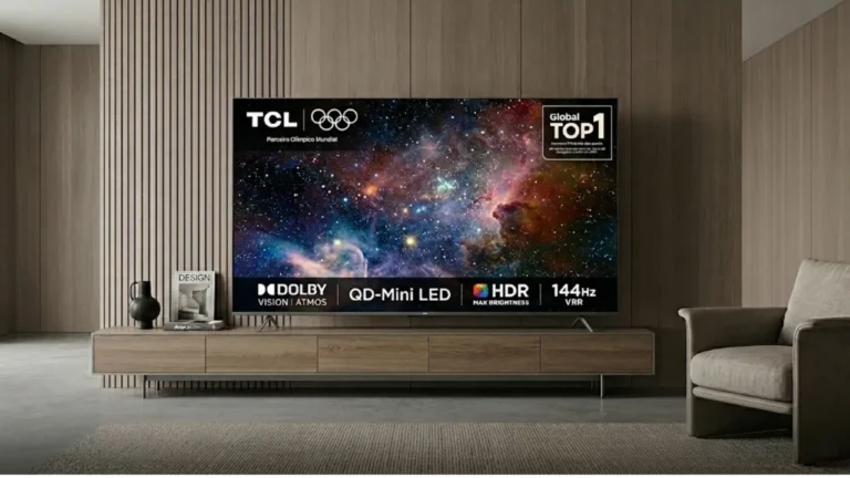 TV TCL C6K instalada sobre um rack de madeira em uma sala de estar sofisticada e minimalista. A tela exibe uma imagem vibrante de uma nebulosa no espaço, destacando selos de tecnologia como QD-Mini LED, Dolby Vision Atmos e 144Hz VRR.