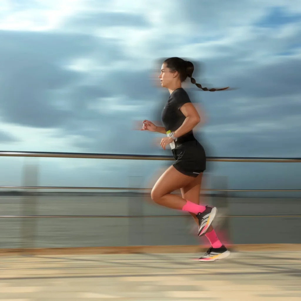 Mulher correndo ao ar livre calçando o tênis Adidas Adizero Drive RC Feminino. A imagem possui um efeito de desfoque de movimento que transmite a sensação de velocidade na passada.