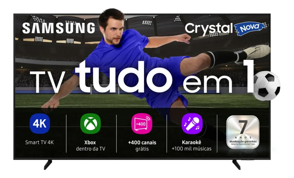 Smart TV Samsung 8100F Crystal UHD, identificada entre as melhores TVs Copa 2026, vista de frente sobre seu suporte. A tela exibe um anúncio promocional vibrante com um jogador de futebol em uma pose de chute acrobático no ar em um grande estádio de futebol lotado à noite, com uma bola de futebol ao seu lado. Acima dele, estão os logos 'SAMSUNG', 'Crystal' e 'Nova'. O texto central grande em português diz 'TV tudo em 1'. Na parte inferior, ícones detalham os principais recursos: 'Smart TV 4K', 'Xbox dentro da TV' (para jogos em nuvem), '+400 canais grátis', 'Karaoke +100 mil músicas' e '7 ANOS Atualização garantida' (para o sistema operacional Tizen).