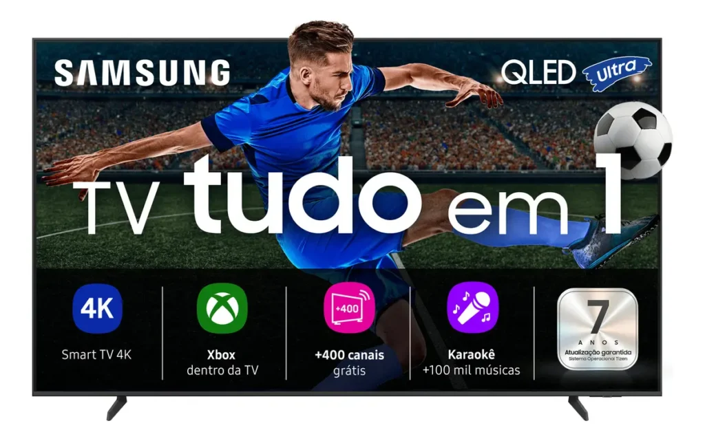 Smart TV Samsung QEF1, identificada entre as melhores TVs Copa 2026 por sua qualidade, vista de frente sobre seu suporte. A tela exibe um anúncio de marketing vibrante com um jogador de futebol chutando uma bola em um estádio lotado. Acima dele, estão os logos 'SAMSUNG' e 'QLED Ultra'. O texto principal e central diz 'TV tudo em 1'. Na parte inferior, ícones detalham recursos como: '4K Smart TV', 'Xbox dentro da TV', '+400 canais grátis', 'Karaokê +100 mil músicas' e '7 ANOS Atualização garantida Sistema Operacional Tizen'.
