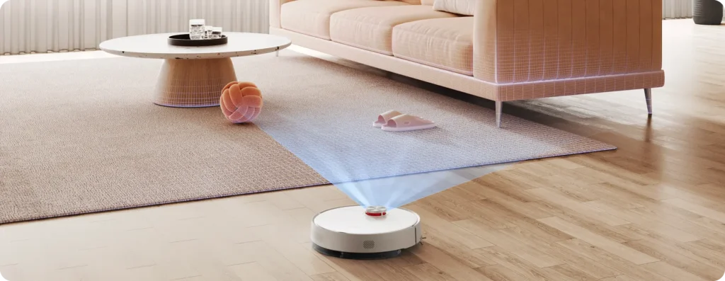 Um robô aspirador xiaomi branco no chão de madeira de uma sala, emitindo um feixe de luz azul do seu sensor superior para escanear o ambiente e identificar obstáculos como um tapete, chinelos e um novelo.