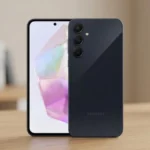 Uma foto em close-up de dois smartphones Samsung Galaxy A35 (vistas frontal e traseira) sobre uma mesa de madeira de carvalho claro em um ambiente de escritório moderno desfocado.