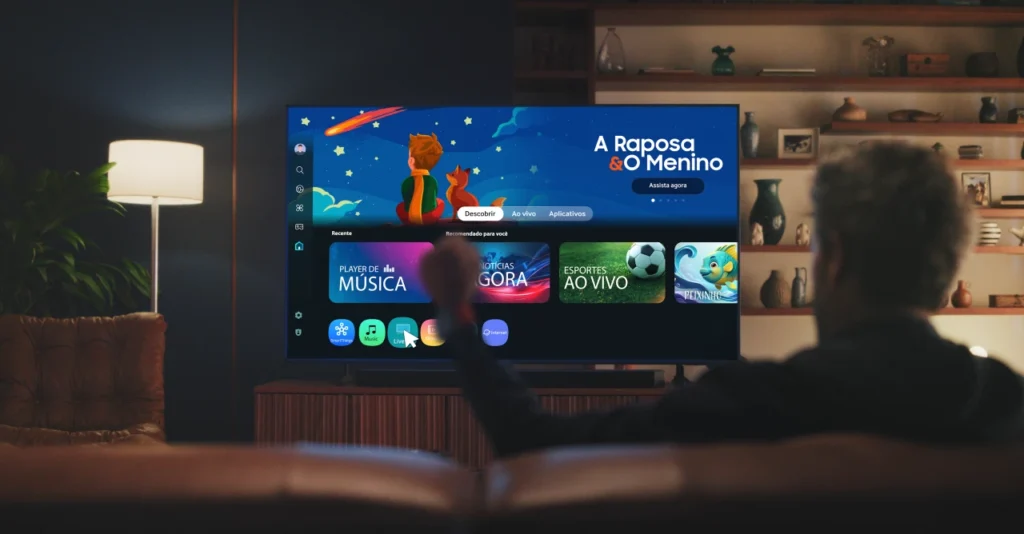 Homem sentado no sofá de uma sala com iluminação aconchegante, controlando uma Smart TV através de gestos com a mão. A tela exibe uma interface inteligente e moderna com diversas opções de entretenimento, destacando o menu 'Esportes Ao Vivo', recurso essencial na busca pelas melhores TVs Copa 2026.